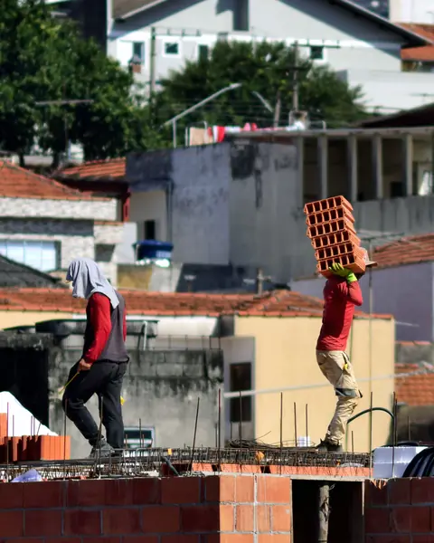 Operários carregando blocos numa obra residencial